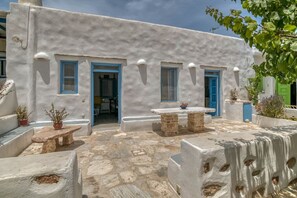 A white building with blue doors and windows, stone flooring, and outdoor seating.