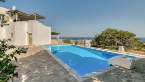 A swimming pool with a stone deck, a white building with a stone facade, and a view of the sea. - Folia House - Overlooking (Aspro Chorio)