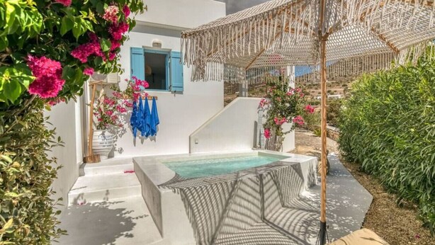 A private outdoor hot tub area with a stone bench, a pergola, and a white building with blue shutters. - Onikos House - South Gem (Aliki)
