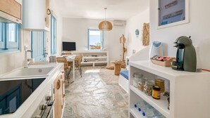 A compact kitchen with a stone floor, white cabinetry, and a dining area with a view. - Onikos House - South Gem (Aliki)