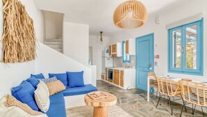 A modern living room with a blue sofa, a wooden coffee table, and a dining area with wicker chairs. - Onikos House - South Gem (Aliki)