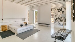 A modern bedroom with a large bed, a bench, and a chair. - Luxury standards in great location (Kostos)