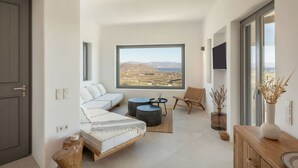 Ein modernes, kompakes Wohnzimmer mit großem Fenster und schöner Aussicht, einer Couch, einem Sessel und einem kleinen Tisch.