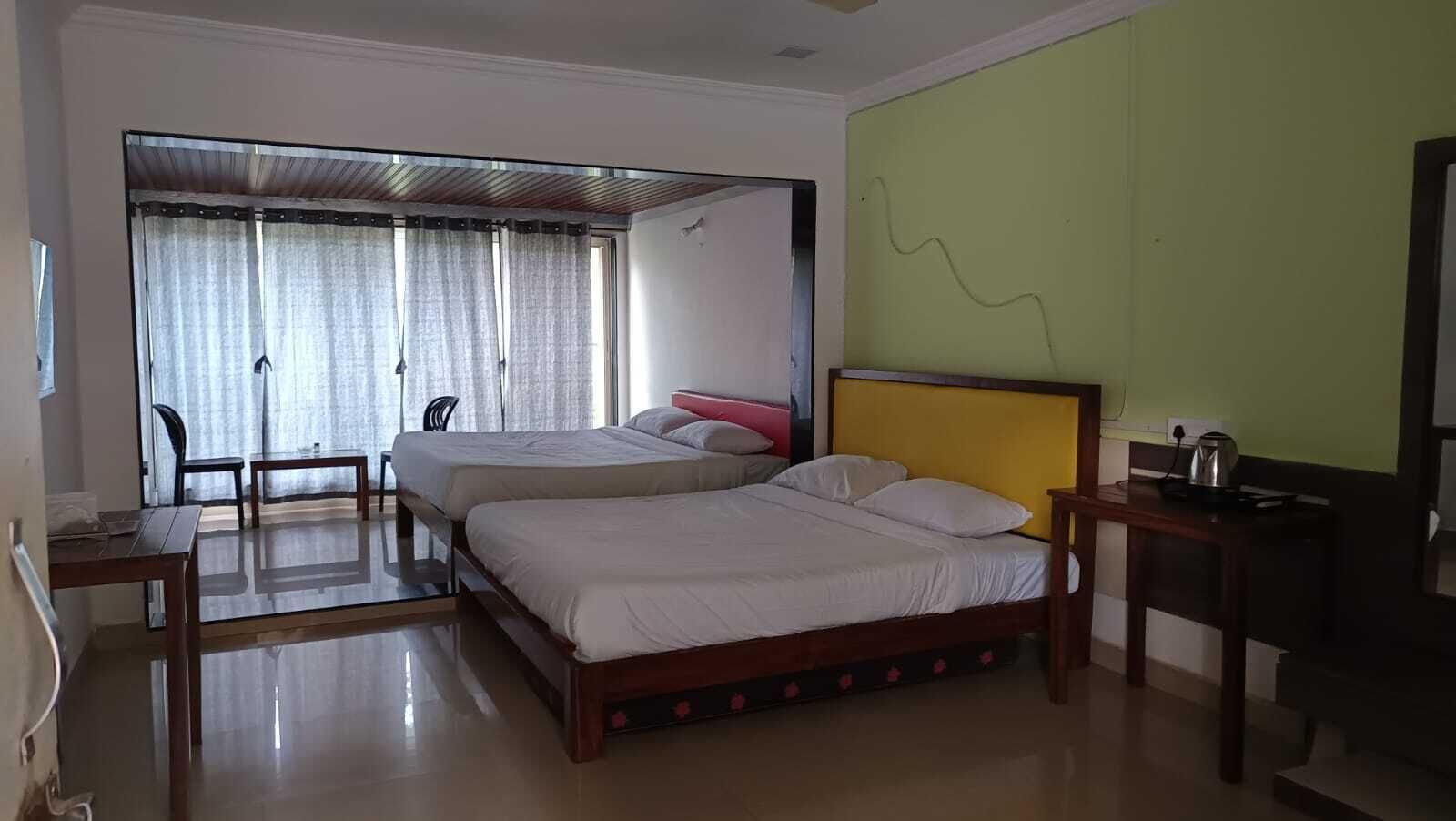 A hotel room with two beds, a desk, a chair, and a kitchenette.