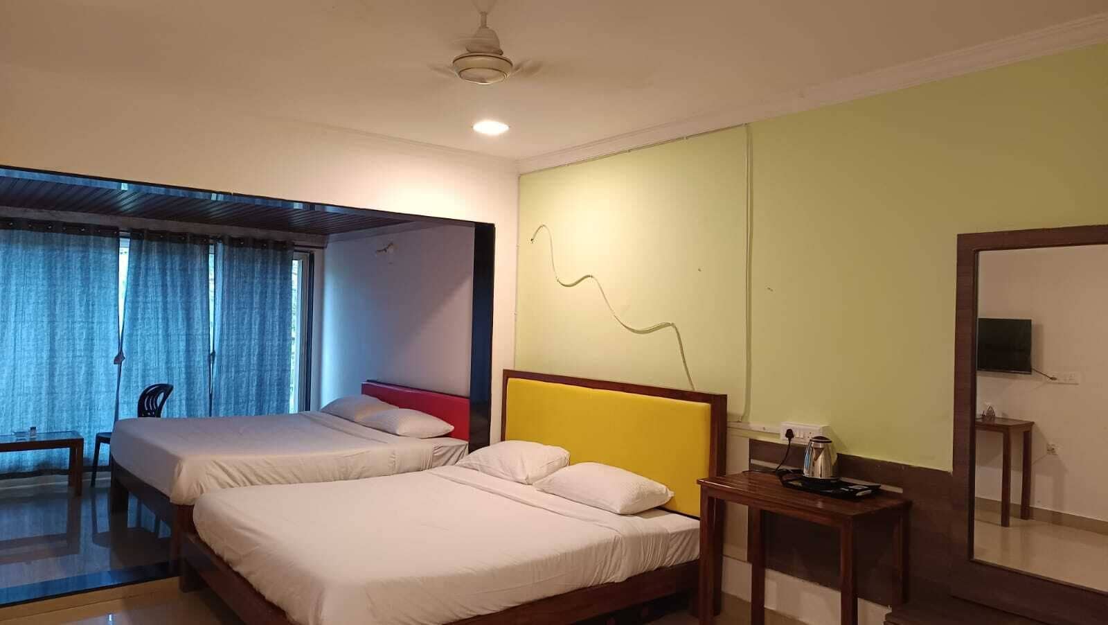 Ein Hotelzimmer mit zwei Betten, einem Schreibtisch, einem Sessel, einem Fernseher und einem großen Spiegel.