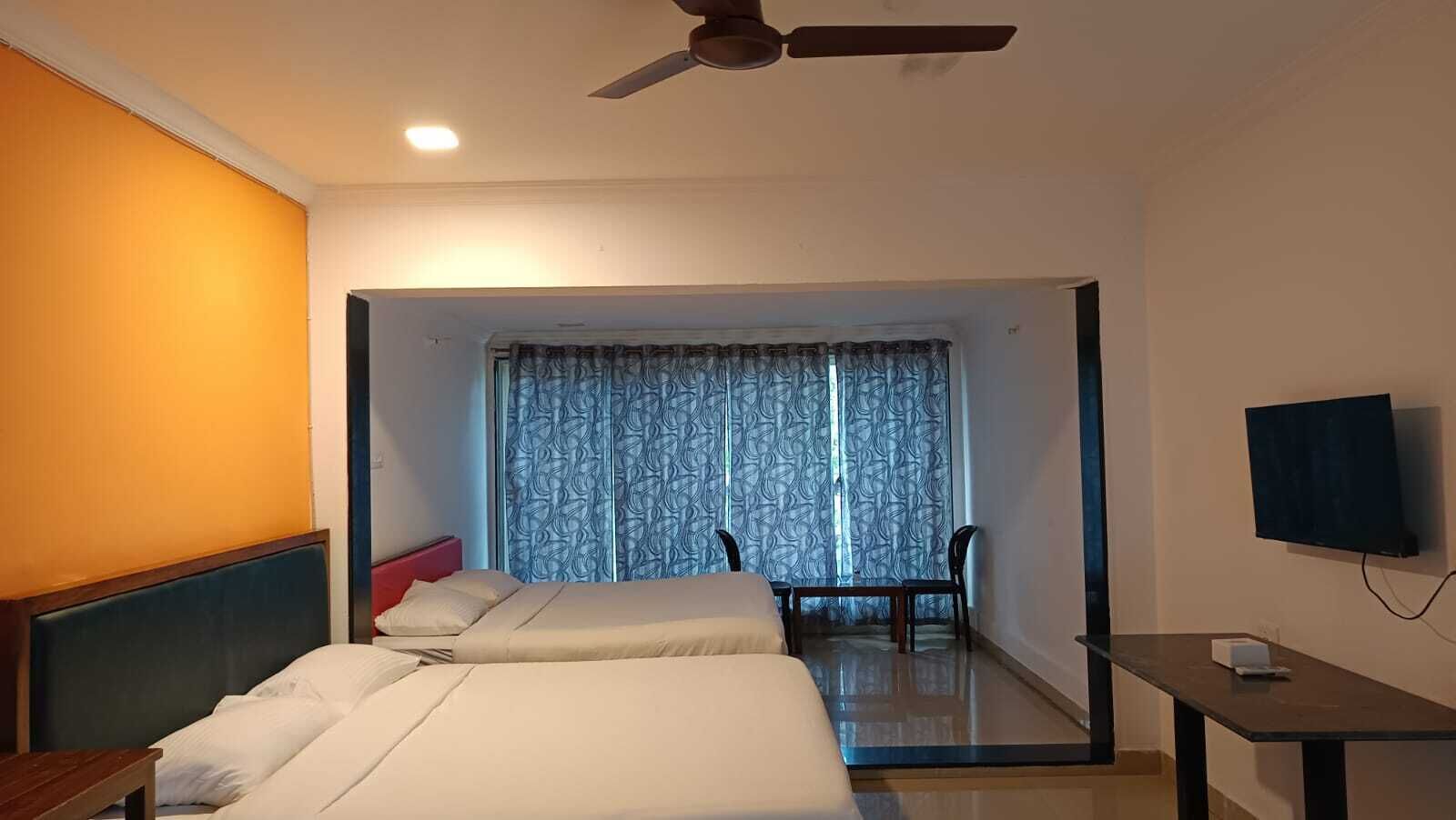 A hotel room with two beds, a ceiling fan, a TV, and a view of a balcony with curtains.
