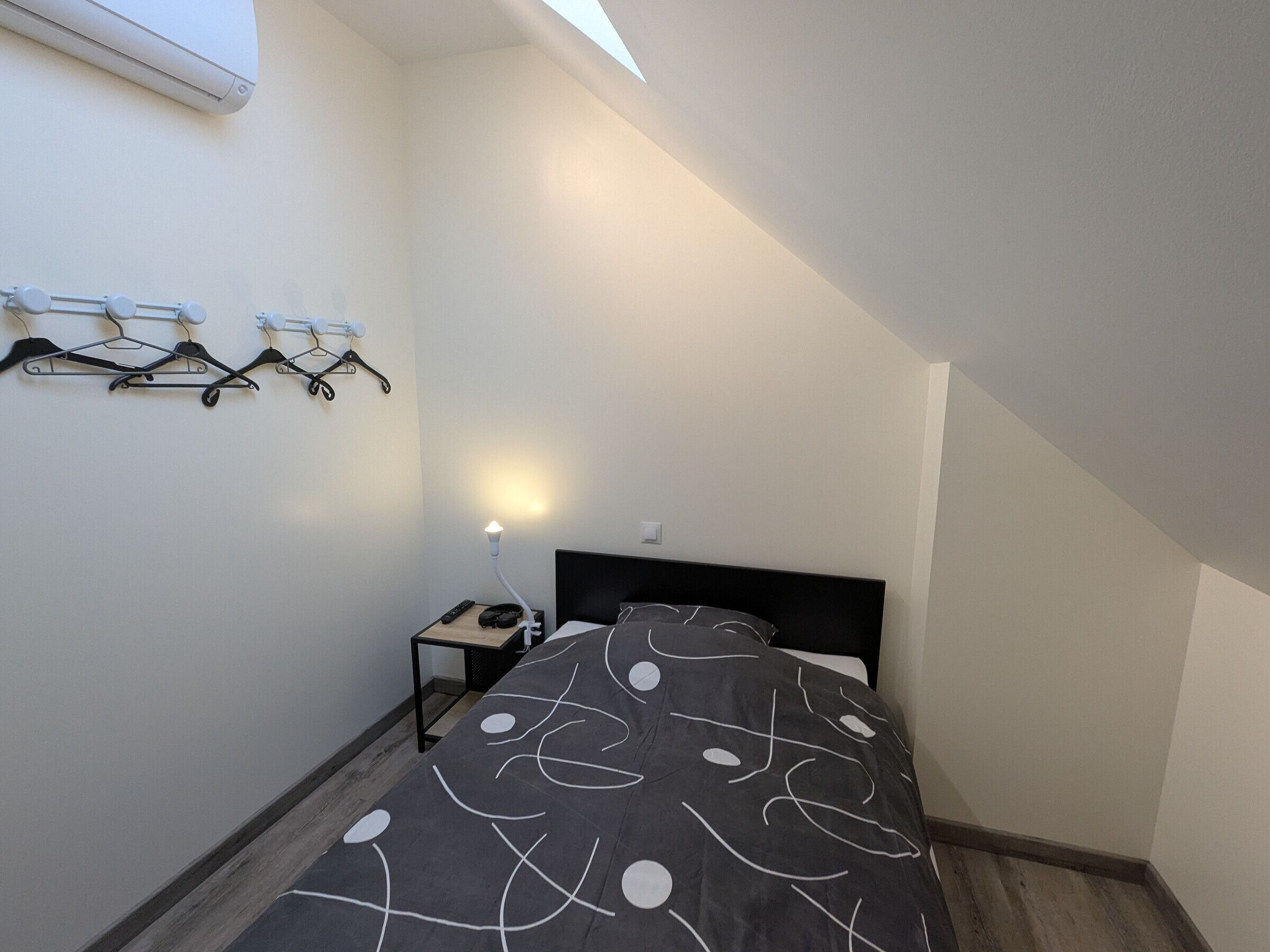Ett litet, modernt sovrum med en säng, ett nattduksbord, en lampa och en takfläkt.