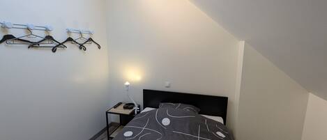 Ett litet, modernt sovrum med en säng, ett nattduksbord, en lampa och en takfläkt.