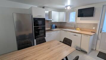 A compact kitchen with a wooden table, white cabinets, a built-in oven, and a TV mounted above the sink.