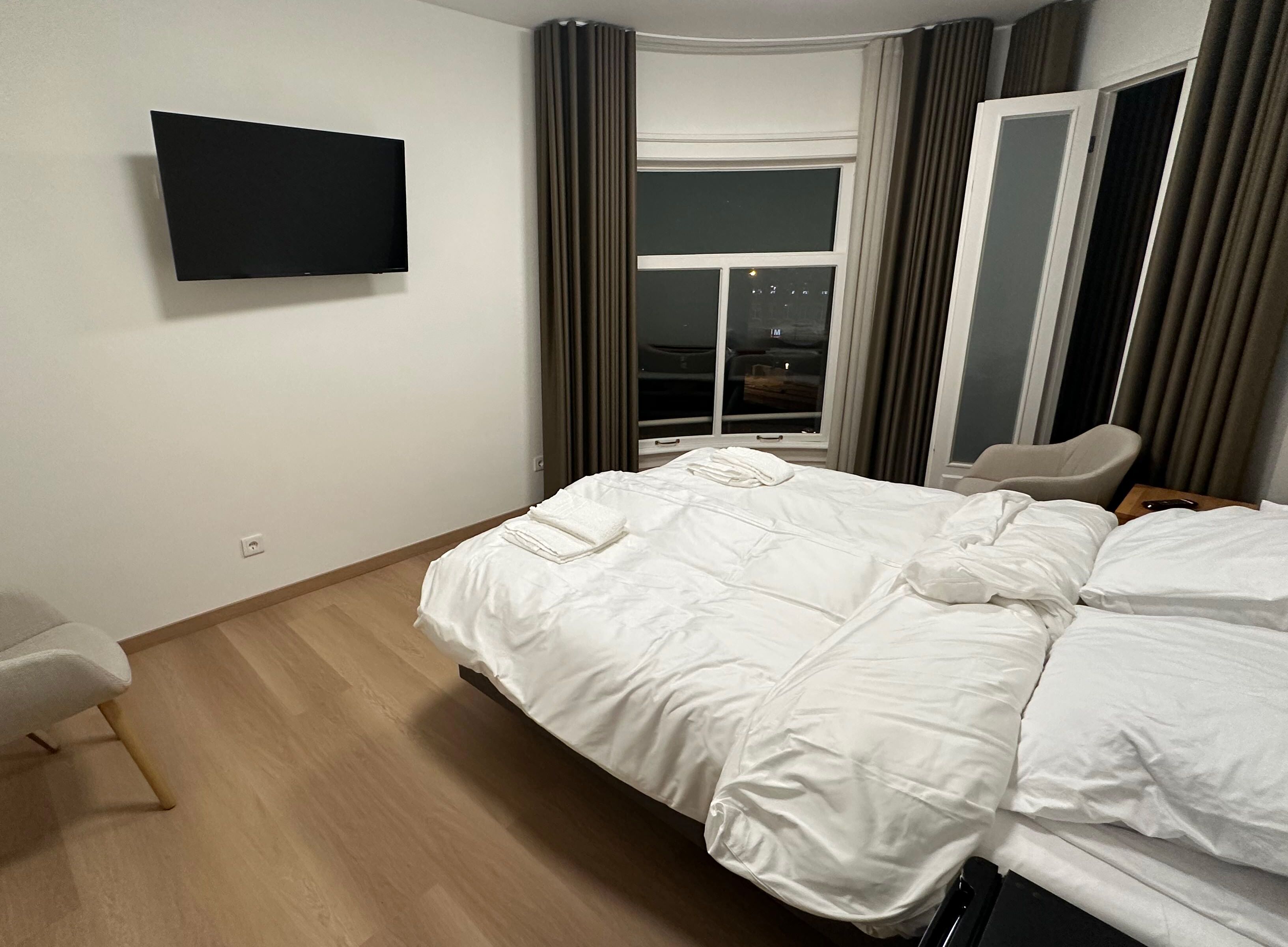 A hotel room with a bed, a chair, a TV, and a window with curtains.
