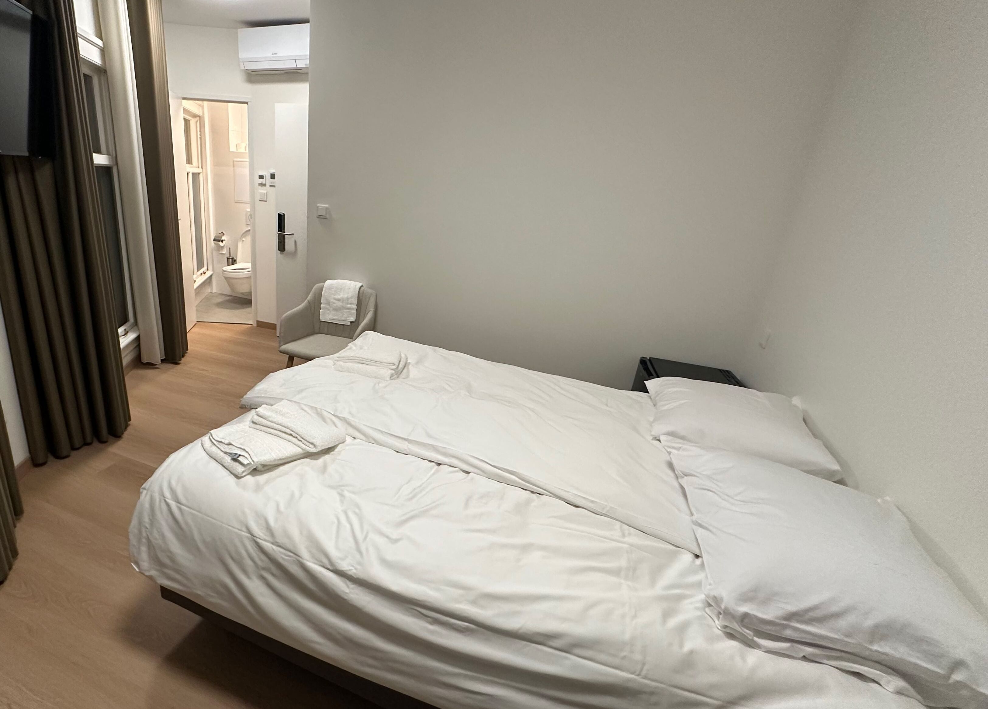 A hotel room with a large bed, a chair, and a bathroom visible in the background.