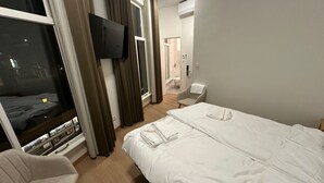 Ein Hotelzimmer mit Bett, Fernseher, Sessel und einem Fenster mit Vorhängen.