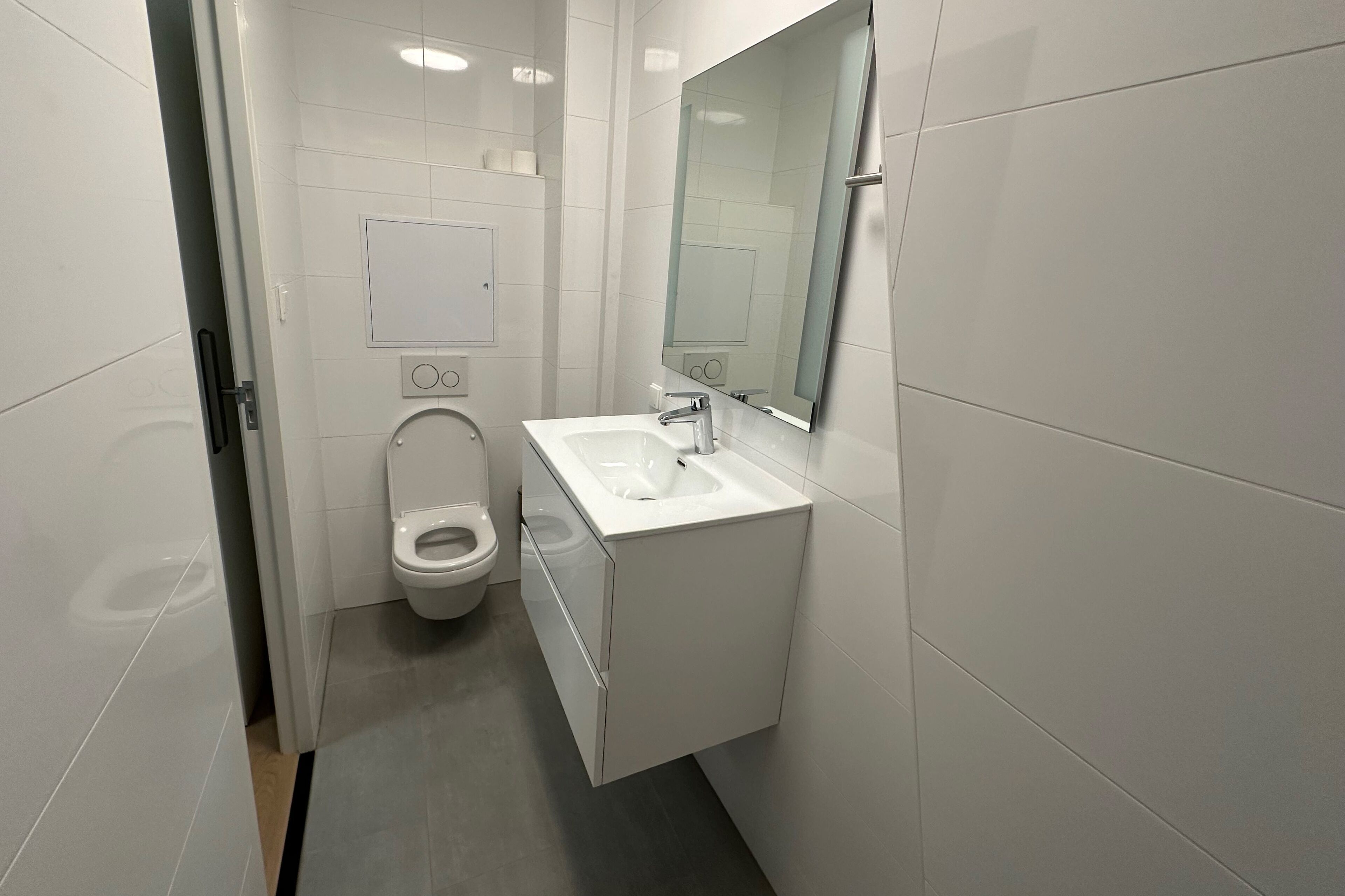 Un baño moderno con inodoro, lavamanos y espejo.