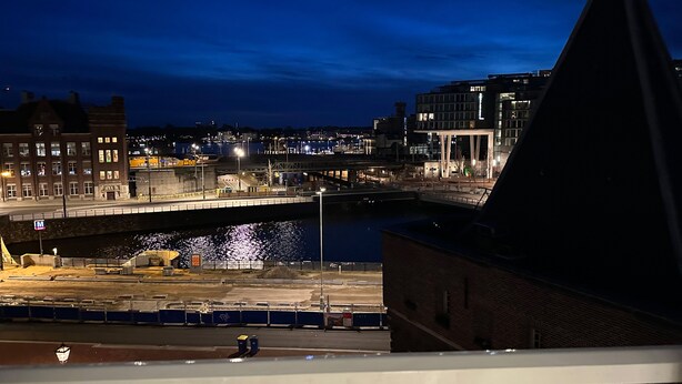 Überblicksaufnahme einer beleuchteten Stadt bei Nacht mit Fluss, Gebäuden und Brücke.