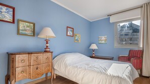A bedroom with a wooden dresser, a bed with white bedding, two bedside tables with lamps, and a window with curtains.