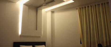 Quarto de hotel com cama bem arrumada, mesa de cabeceira com abajur e janela com cortinas.