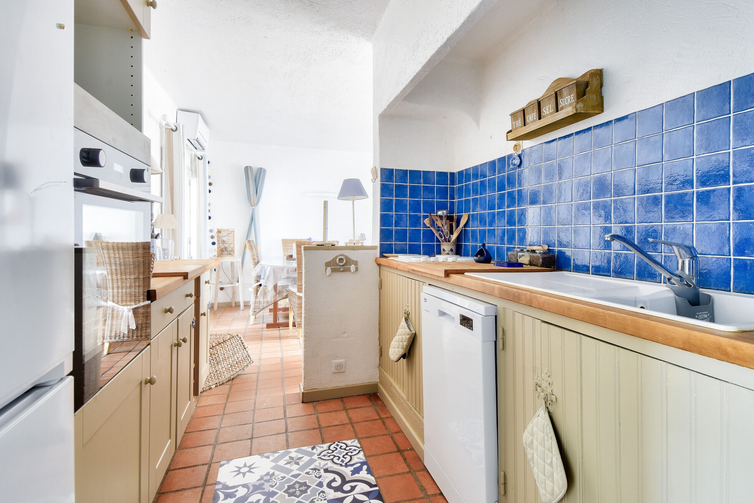 A kitchen with a blue tiled backsplash, a wooden countertop, and a white sink.