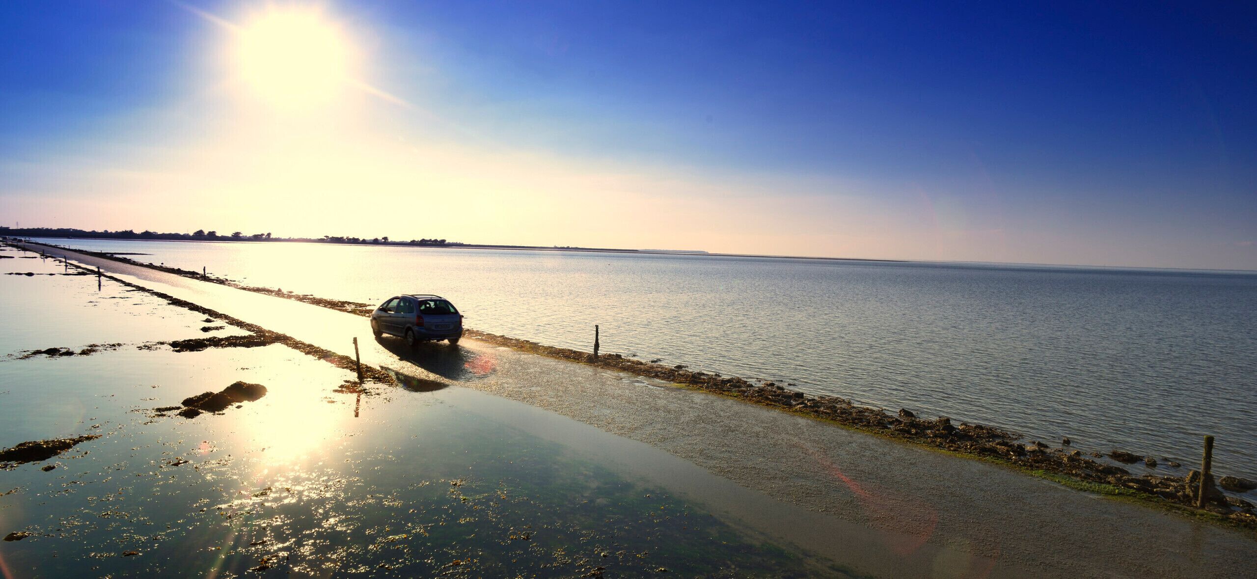 Ein Auto fährt auf einer Küstenstraße mit Blick auf das Meer und einen klaren Himmel.