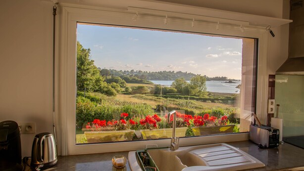 A kitchen with a large window overlooking a scenic landscape, a sink, and a toaster.