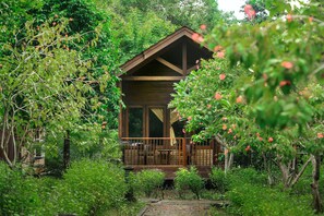 A wooden cabin surrounded by lush greenery and a wooden deck. - Plengkung Lodge G-land (Kalipait)