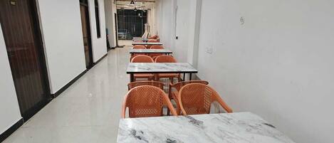 A long corridor with tables and chairs, a wooden ceiling, and a tiled floor.