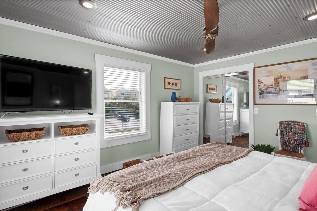 A bedroom with a bed, a television, a dresser, and a window with blinds.