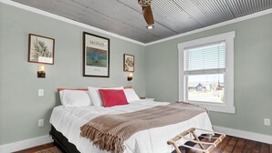 A bedroom with a bed, a window, and artwork on the wall.