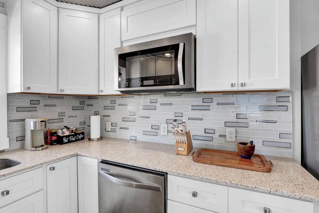 Cozinha com armários brancos, micro-ondas de aço inoxidável e painel de azulejos.