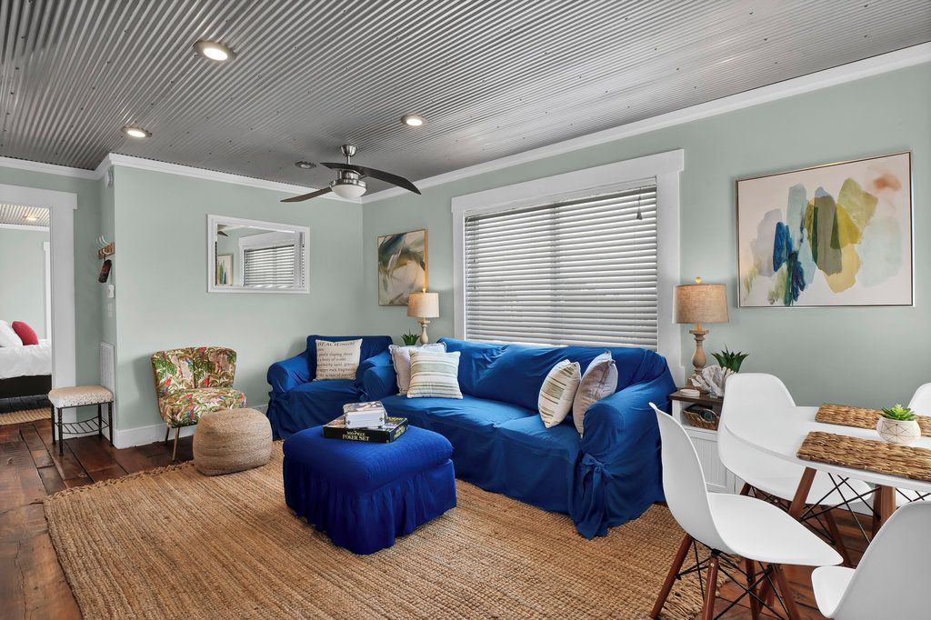A living room with a blue sofa, white chairs, a dining table, and a ceiling fan.