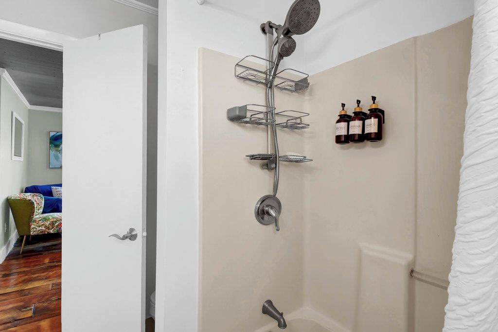 A shower with a rain showerhead, a handheld showerhead, and a handheld massager. There are three bottles of shampoo on the wall.