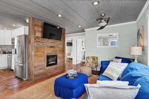 A modern living room with a fireplace, a sofa, and a television mounted on a wooden wall. - Coastal Cottage - Upscale 2 BR Condo at Mini Golf (Topsail Beach)