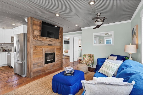 A modern living room with a fireplace, a sofa, and a television mounted on a wooden wall. - Coastal Cottage - Upscale 2 BR Condo at Mini Golf (Topsail Beach)