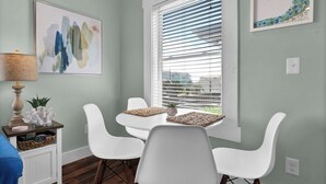 A dining area with a table and chairs, a window with blinds, a lamp, and a wall with a framed artwork.