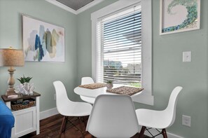 A dining area with a table and chairs, a window with blinds, and a wall with artwork.