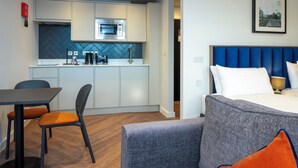 Une chambre d’hôtel compacte comprenant un coin cuisine, un espace repas et un lit avec une tête de lit bleue.