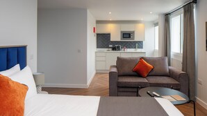 Une chambre d’hôtel avec un lit, un canapé, une petite table et, au fond, un coin cuisine.
