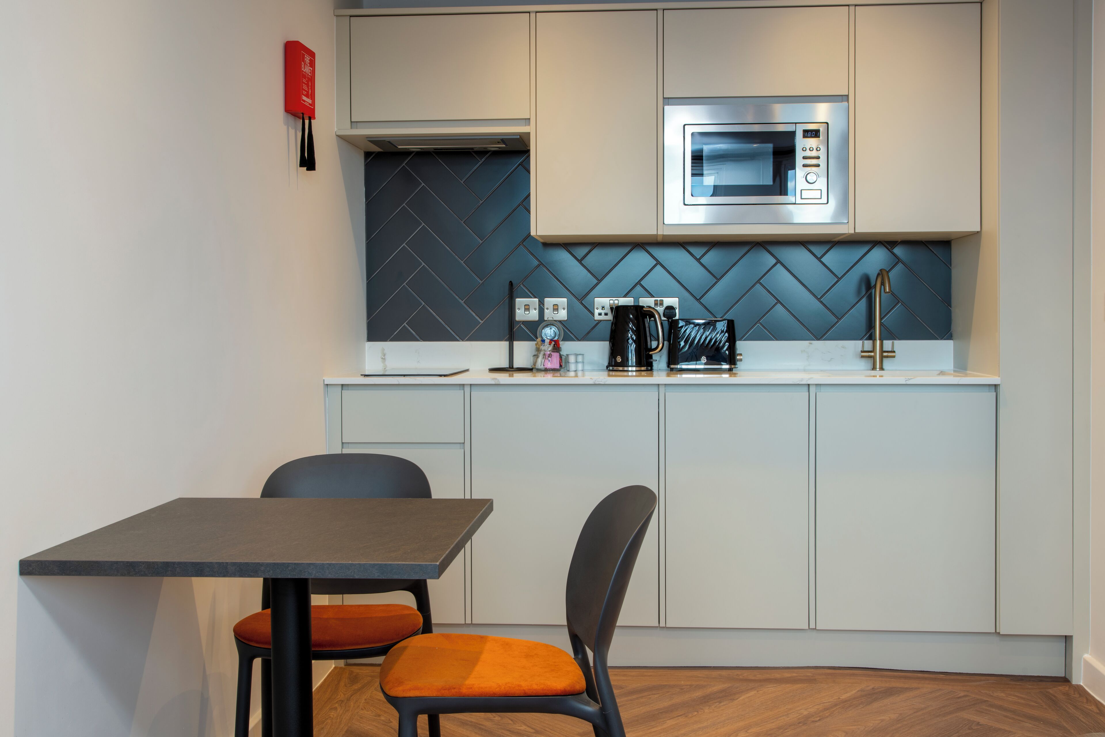 A modern kitchen with a microwave, coffee maker, and a red fire extinguisher. There is a table with two chairs.