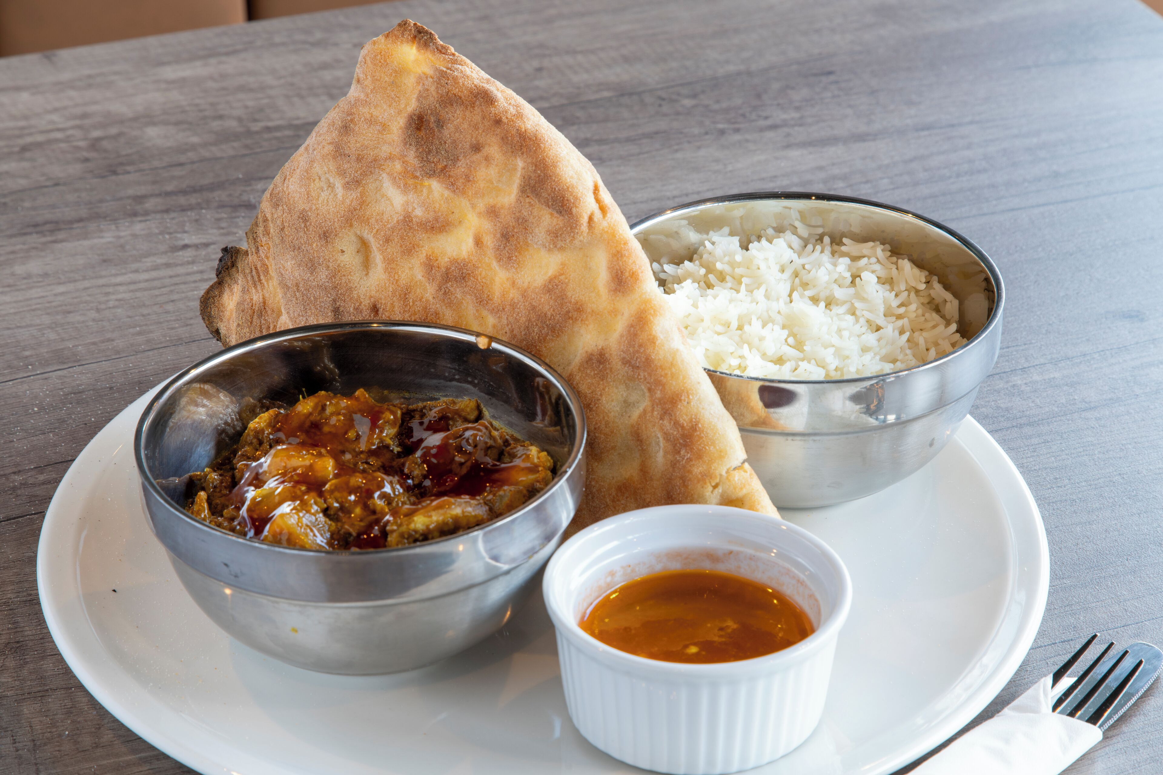 Un plato con pan naan, arroz, un tazón de curry y un recipiente pequeño con salsa.