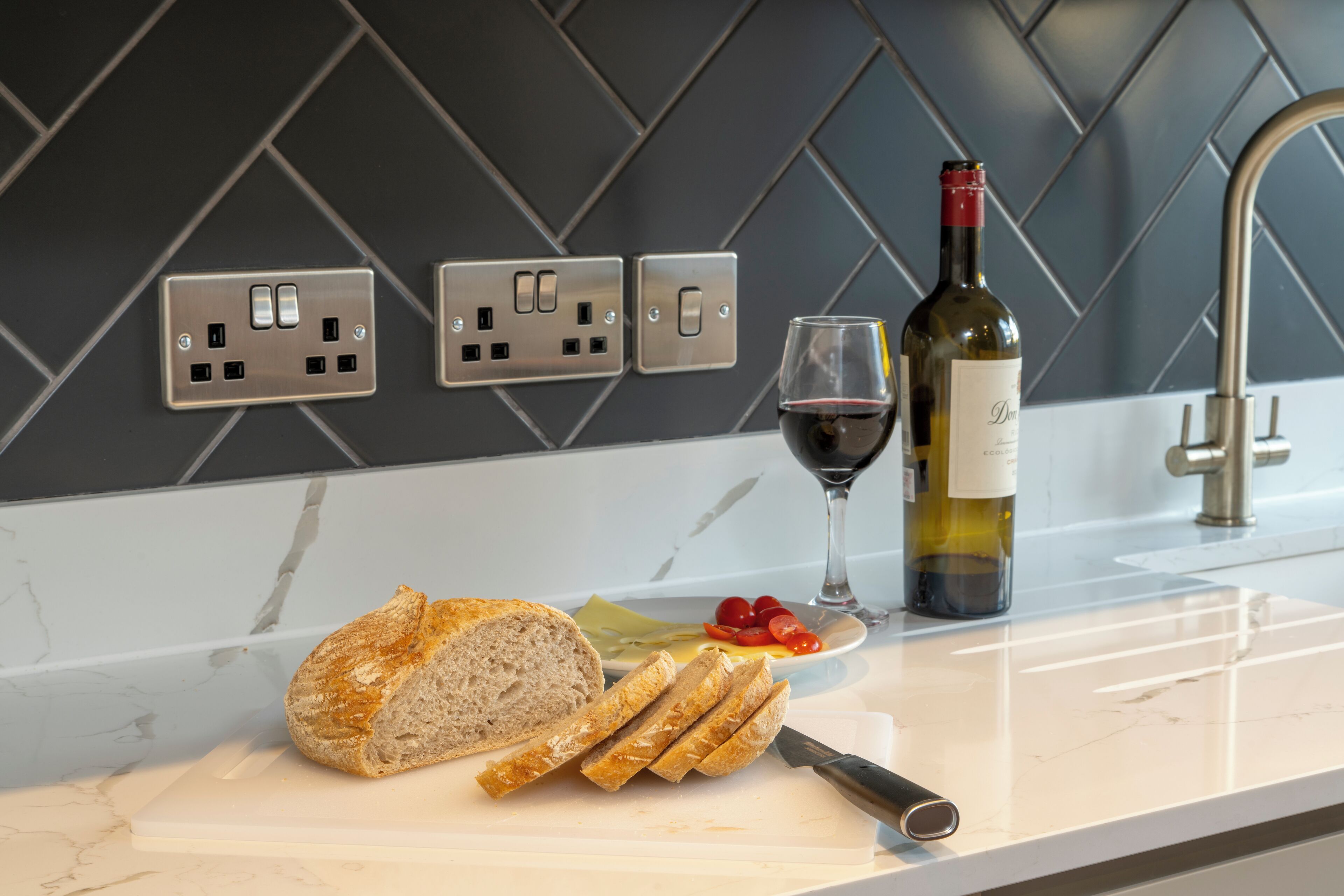 A kitchen counter with a loaf of bread, a bottle of wine, and a glass of red wine.
