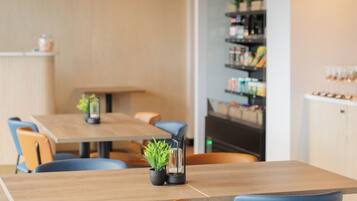 A modern dining area with a wooden table and chairs, a small plant, and a shelf with various items.