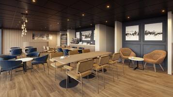 A modern conference room with a long table, blue and tan chairs, and a kitchen area in the background.