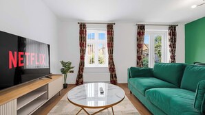 A living room with a TV, a green sofa, a round coffee table, and curtains. - 3 Bed Pendlebury Home | Free Parking | Pets (Pendlebury)