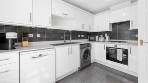 A modern kitchen with white cabinets, a dishwasher, a washing machine, a microwave, and a stove. - 3 Bed Pendlebury Home | Free Parking | Pets (Pendlebury)