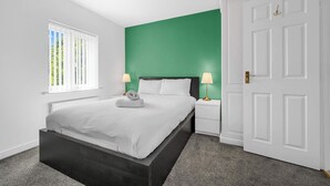 A bedroom with a bed, bedside tables, a window with blinds, a green accent wall, and a white door. - 3 Bed Pendlebury Home | Free Parking | Pets (Pendlebury)
