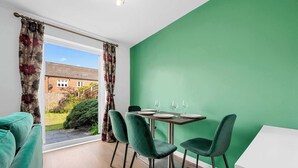 A dining area with a table set for four, green chairs, a green wall, and a view of a garden through a window. - 3 Bed Pendlebury Home | Free Parking | Pets (Pendlebury)