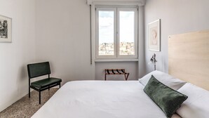 A bedroom with a bed, a chair, a bench, a window, and two framed pictures on the walls. - Amazing Metro Piramide Station (Roma)