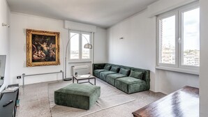 A modern living room with a green sectional sofa, a small ottoman, a coffee table, and a painting on the wall. - Amazing Metro Piramide Station (Roma)