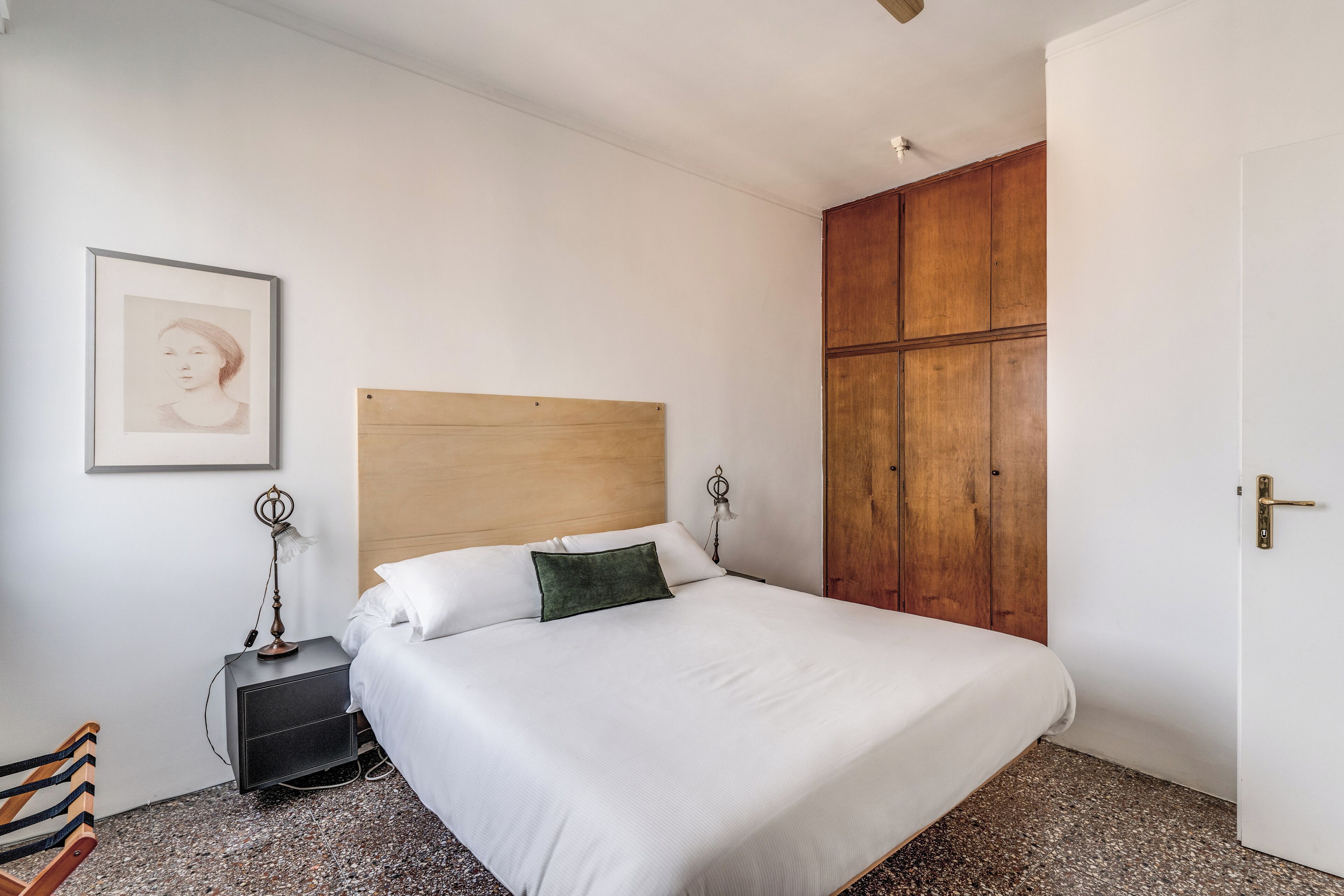 Un lit bien fait, avec une tête de lit en bois, une table de chevet avec une lampe et un tableau encadré accroché au mur.
