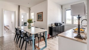 A modern kitchen with a dining area, featuring a large table, chairs, a black cabinet, a vase with flowers, and a window with a view. - Amazing Metro Piramide Station (Roma)