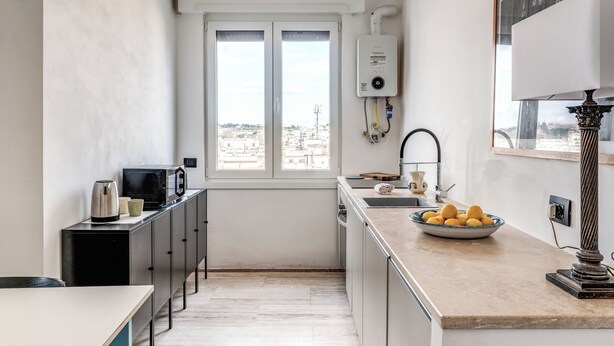 A compact kitchen with a view of the city, a water heater, and a bowl of lemons on the counter. - Amazing Metro Piramide Station (Roma)